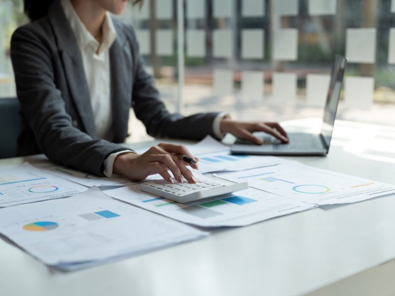 Close up of business woman or accountant working on calculator to calculate business data, accountancy document and laptop computer at office, business concept.